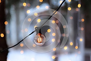 Close-up view of illuminated retro light bulb hanging outdoors and lighting garlands as Christmas decoration in cold day of