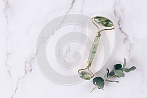 Close up view of jade facial roller gua sha on white marble table background. Facial massage kit for lifting massage therapy made