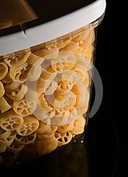 Close up view of jar full with Rotelle Wagon wheel-shaped pasta against dark background