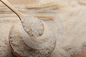Close up view of jasmine rice in a wooden bowl,  spoon and  ear of rice on wooden background
