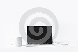 close up view of laptop with blank screen, earphones and white mug isolated on white