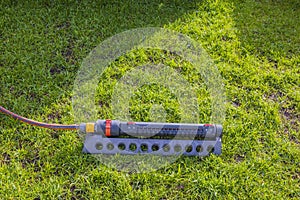 Close up view of lawn irrigation system with hose lying on green grass in garden.