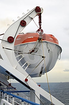 Close-up view of lifeboat on deck of a cruise ship. Orange lifeboat on mounting bracket.