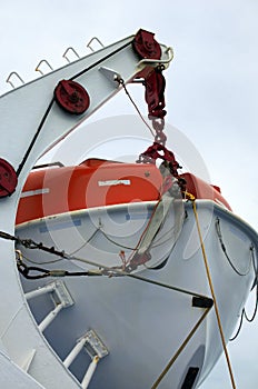 Close-up view of lifeboat on deck of a cruise ship. Orange lifeboat on mounting bracket.