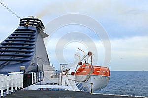 Close-up view of lifeboat on deck of a cruise ship. Orange lifeboat on mounting bracket.