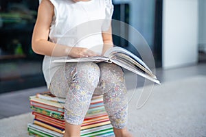 Close up view of Little girl is sitting on stack of children& x27;s books and leafing through a book with fairy tales