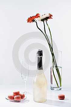 close up view of macarons, empty glass, bottle of champagne and bouquet of gerbera flowers