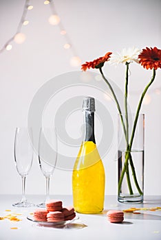 close up view of macarons, empty glasses, bottle of champagne and bouquet of gerbera flowers