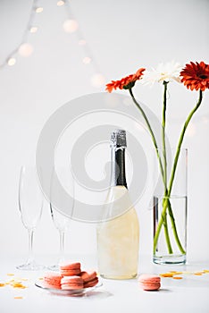 close up view of macarons, empty glasses, bottle of champagne and bouquet of gerbera flowers