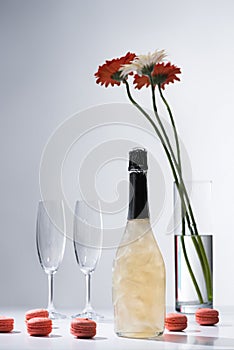 close up view of macarons, empty glasses, bottle of champagne and bouquet of gerbera flowers