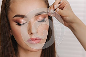 Close up view of make-up artist puts false eyelashes using tweezers. Background of white folding screen