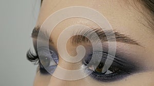 Close up view of makeup artist makes models smoky eyes with the help of special brush blue eyeshadow, eyes and eyelashes