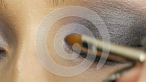 Close up view of makeup artist makes models smoky eyes with the help of special brush blue eyeshadow, eyes and eyelashes