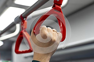 Close up view of male hand holding a looped handle in urban public transportation. People holding a handle in a train