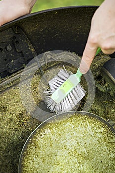 Close up view of man hand brushing off layer of wet grass stuck under automated lawnmower, maintenance concept.