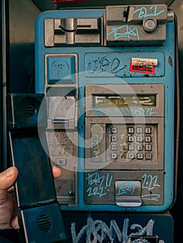 Man hand holding the telephone of an old public phone booth