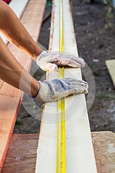 Close up view of a man hands measuring wooden plank with a tape line
