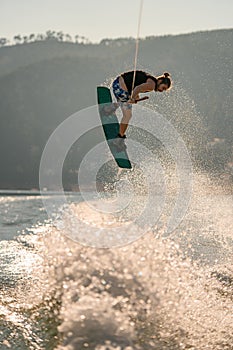 Close-up view of man holding a rope and jumping in the air with wakeboard