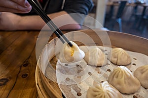 Close up view of a man picking up xiao long bao from a steamer basket inside a restaurant