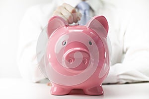 Close up view of man putting coin to pink piggy bank, isolated white background