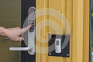 Close up view of man`s hand dialing code on digital lock of entrance door.