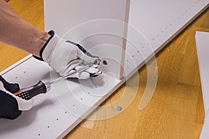 Close up view of man`s hands assembling white furniture in an apartment.