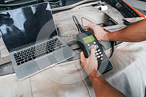Close up view of man`s hands that holding device for testing automobile in salon