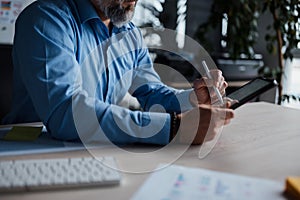 Close up view of the man in shirt touching tablet screen with stylus while sitting at the table