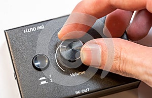 Close-up view of a mans hand turning up adjusting the volume knob on a modern audio device. Making audio output quieter or louder