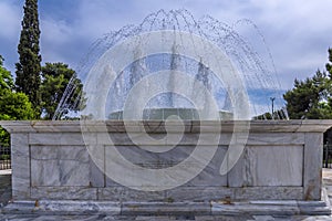 Close up view of the marble fountain gushing water in front of the Zappeion Hall neo-classical building in the National Garden par