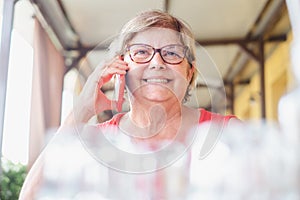 Close up view on a mature lady sitting at the restaurant table while talking at mobile phone. Attractive woman with smiling