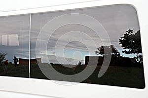 Close-up view of a minibus and cars standing on the shore of a lake. The reflection in the windows of the car.