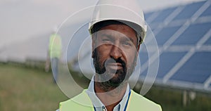 Close up view of mixed raced male engineer in hard helmet looking to camera. Bearded serious man in uniform standing at