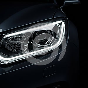 A close-up view of a modern car headlight in a dimly lit setting. The headlight features