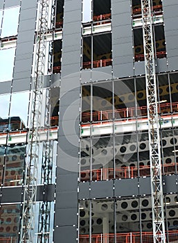 Close up view of a modern construction site with hoists running up the tall building with steel girders with black panels and wind