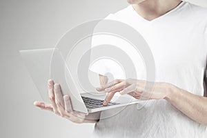 Close-up view of modern laptop in man`s hands, guy wearing white t-shirt, working on portable computer. White background in studio