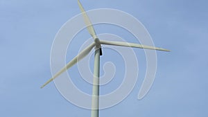 Close-up view of a modern windmill against a blue sky. The white blades of the wind turbine. Clean and renewable energy