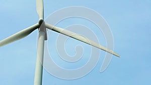 Close-up view of a modern windmill against a blue sky. The white blades of the wind turbine. Clean and renewable energy