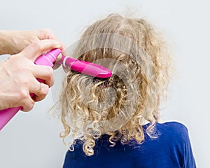 Close up view of mother hands spray curly hair balm on to girl child hair to help combing messy curly hair concept.