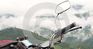 Close up view of a motorbike with backpack in the background of foggy mountains