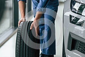 Close up view. Moving the tire. Man in blue uniform is working in the car service