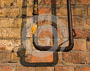 Close up view of an old rusty gas pipe with a faucet. Red brick on a peeling wall.