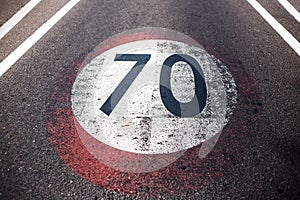 Close-up view of old shabby speed limit sign with 70 km per hour, painted on asphalting road.