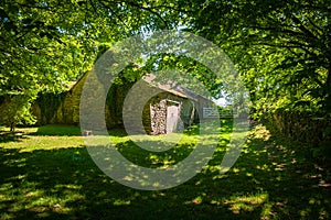 Close-up view of an old stone barn in the shade of trees.