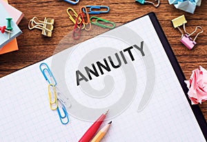 A close-up view of an open notebook with the word ANNUITY clearly written on its lined pages, set against a business background