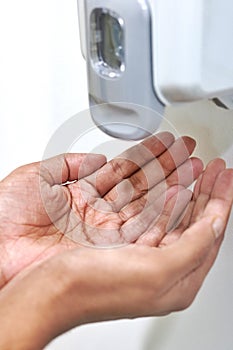 Close up view of open palm under an automatic wall mounted sanitiser dispenser.