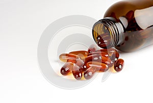 Close-up view of orange pills or lecithin capsules in a brown glass bottle on a white background, with space for text