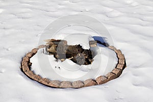 Close up view of an outdoor fire pit with logs, covered in white snow in winter