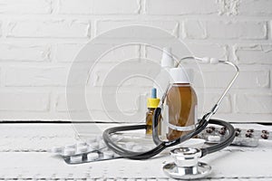 Close up view over a white wooden table with syrip, pills, capsules, sprays, stethoscope and thermometer on it. Flu and seasonal d