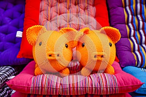 Close-up view of a pair of funny little pigs knitted with orange wool among colourful chairs